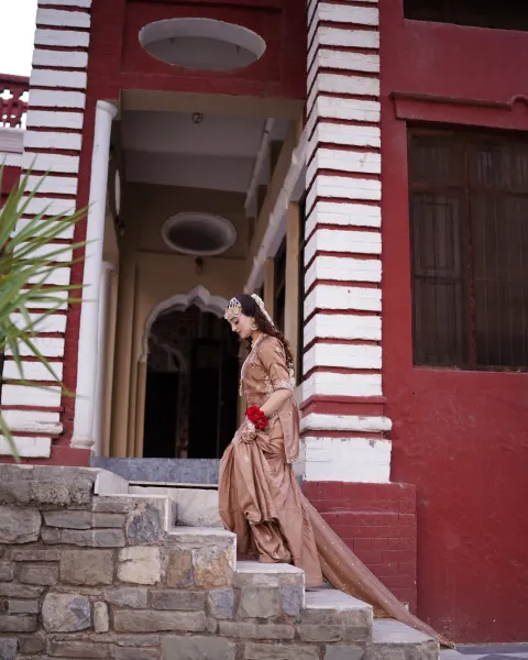 A Pakistani bride walking down rustic stone steps outside a red and white colonial-style heritage building while looking down, captured by AM Productions.