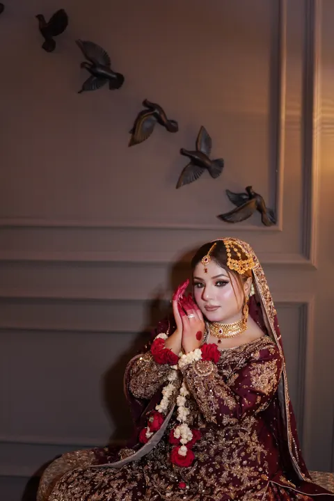 A stunning South Asian bride wearing a heavily embellished deep maroon and gold bridal dress with traditional jewelry and floral jewelry accents — Islamabad & Rawalpindi photography by AM Productions.