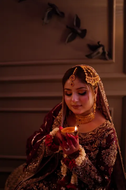 An Instagram reel cover of a South Asian bride in a maroon and gold outfit holding a lit diya, featuring traditional jewelry and festive decor — Islamabad & Rawalpindi photography by AM Productions.