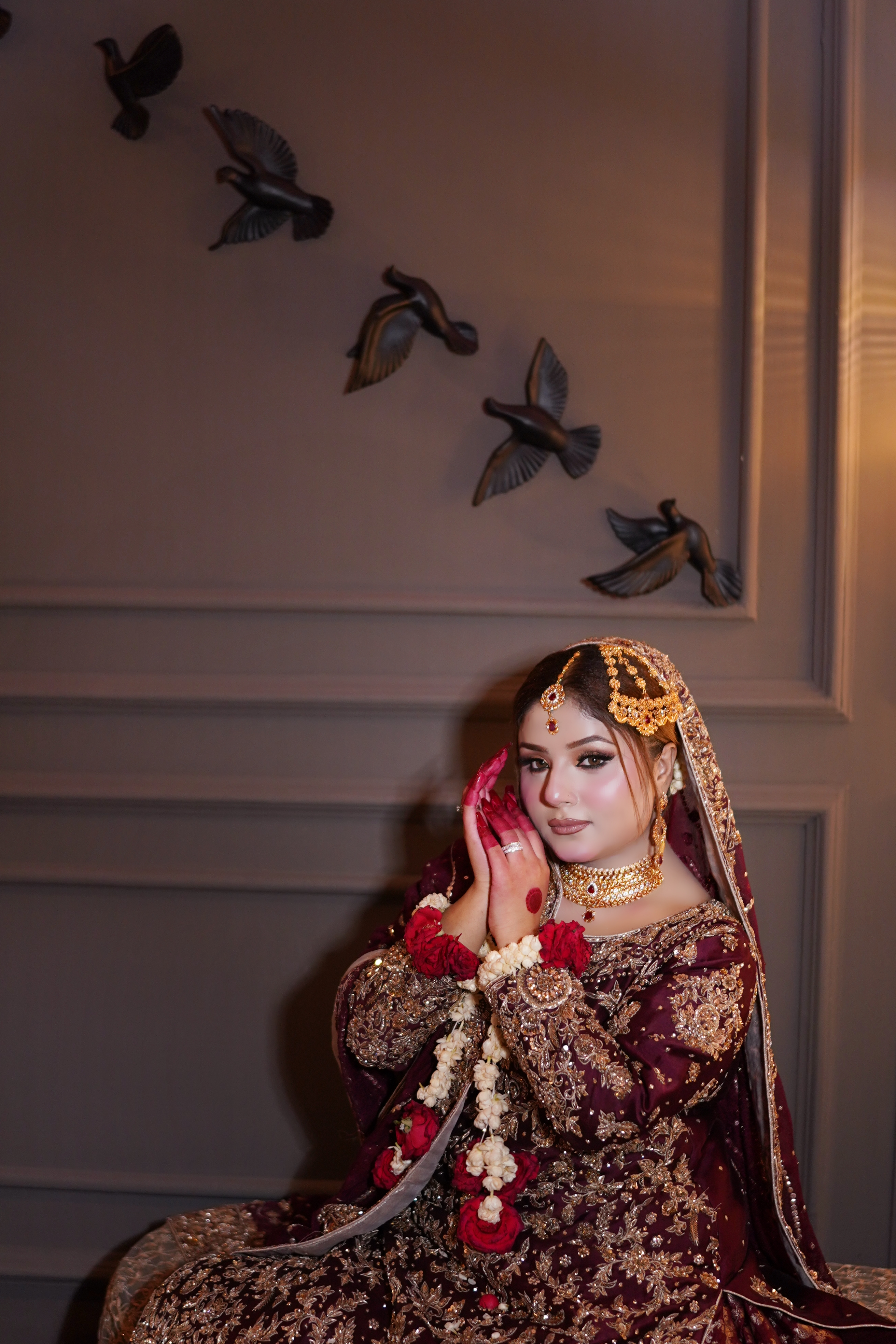 A stunning South Asian bride wearing a heavily embellished deep maroon and gold bridal dress with traditional jewelry and floral jewelry accents — Islamabad & Rawalpindi photography by AM Productions.