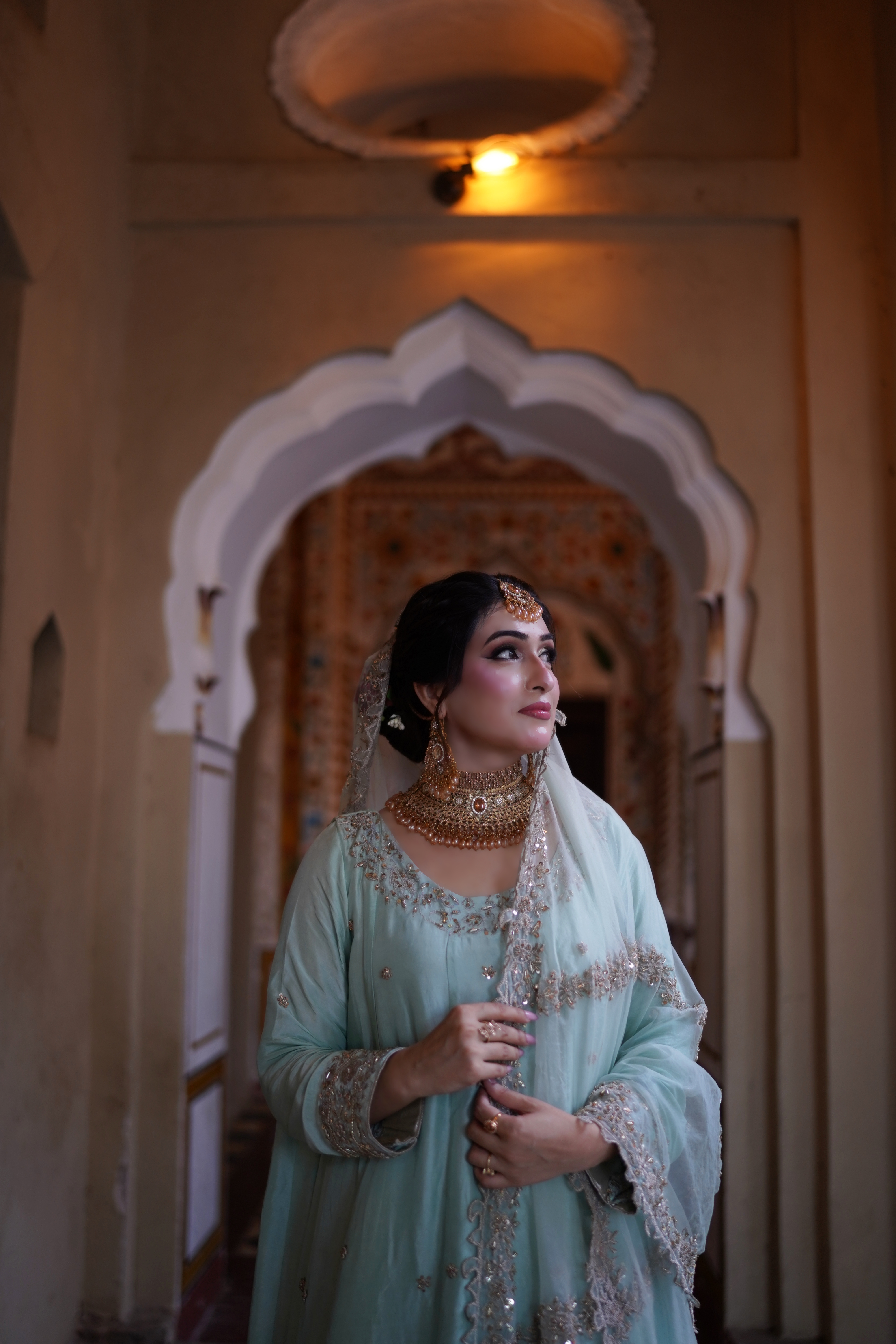 Cinematic close-up bridal portrait of a bride in mint green traditional attire under an arched hallway, photographed by AM Productions in Islamabad and Rawalpindi.
